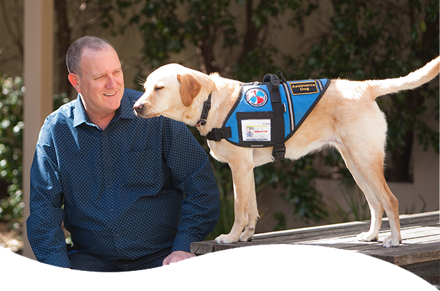 Phil Hazell sitting at a picnic table and his service dog standing on the table next to him.